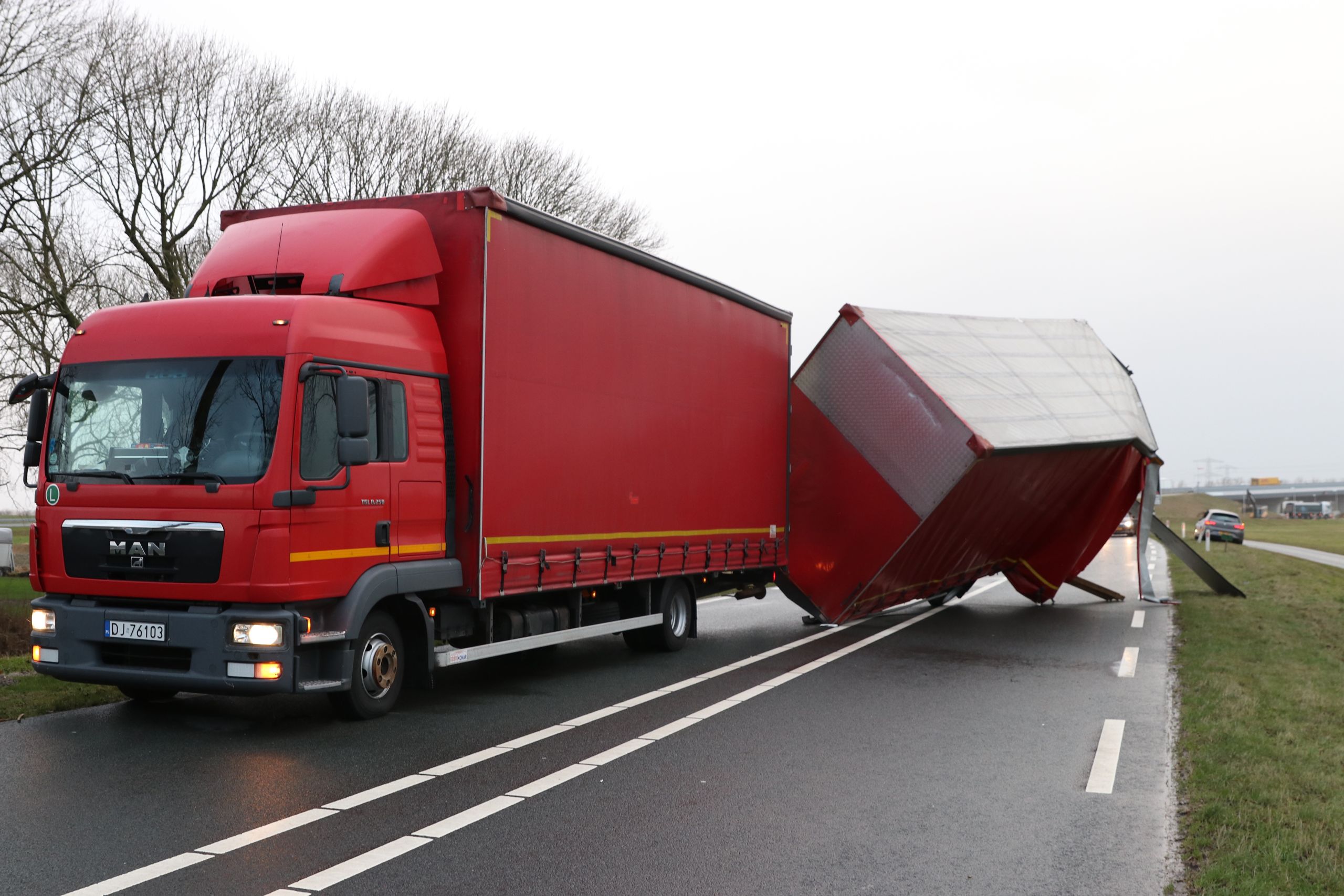Een door de storm gekantelde vrachtwagenaanhanger, donderdag bij Kampen. De aanhanger kwam gedeeltelijk op een passerende auto terecht.