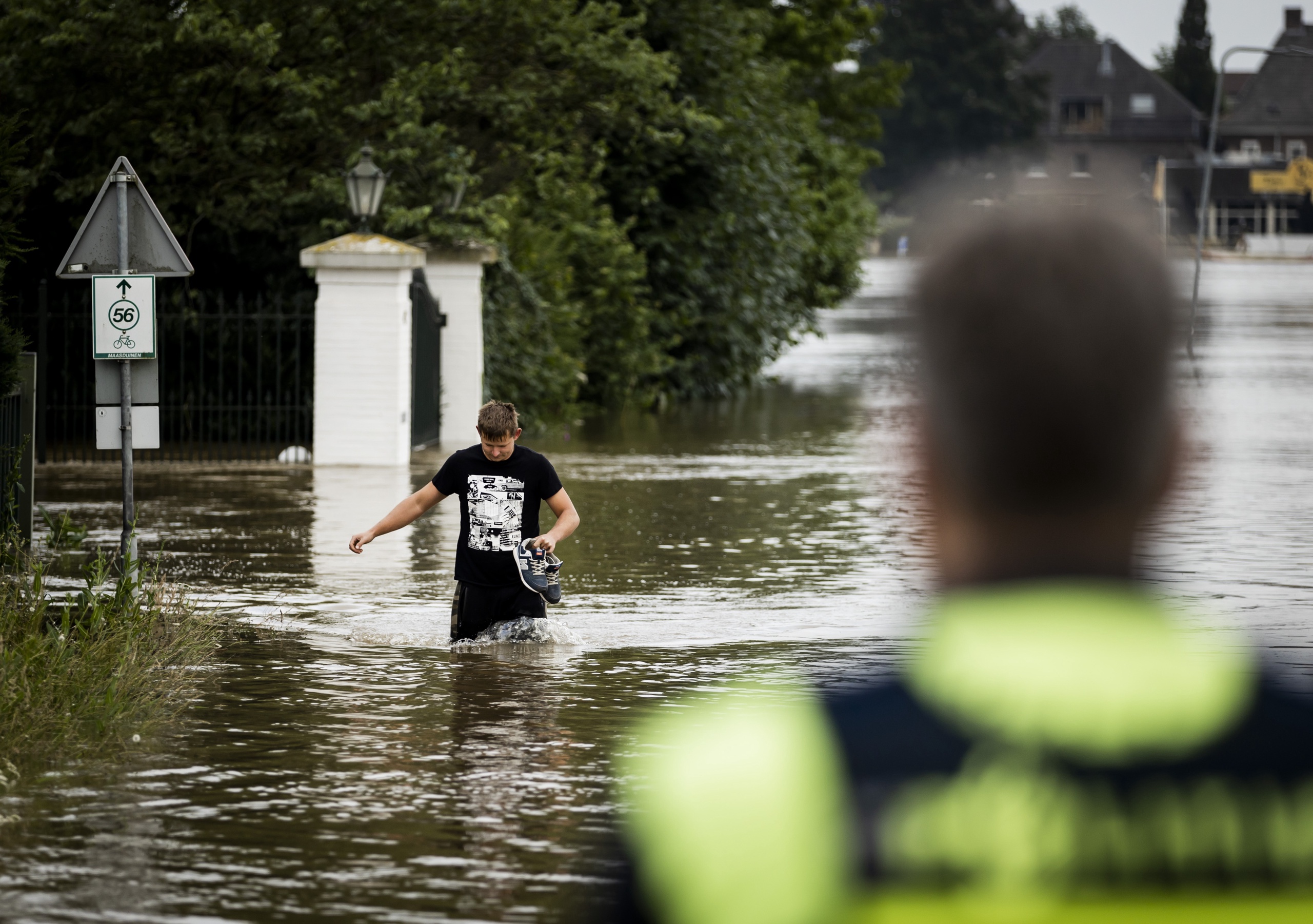 Een man verlaat, onder toeziend oog van de ME, een onder water gelopen woning in Arcen. De hevige regenval en overstromingen in Noord-Limburg hebben vorig jaar voor veel schade gezorgd.