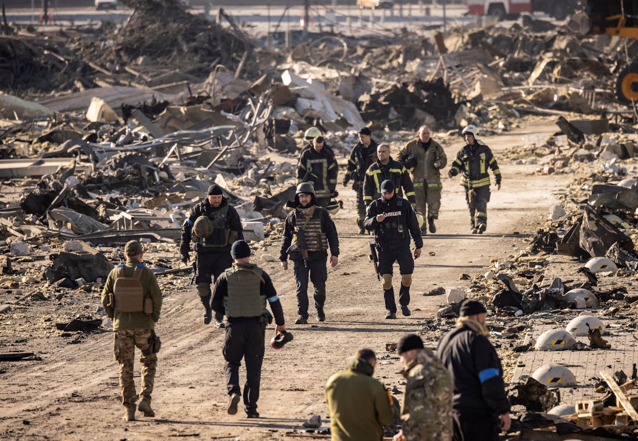 Reddingswerkers en militairen lopen rond in een gebied dat net gebombardeerd is.