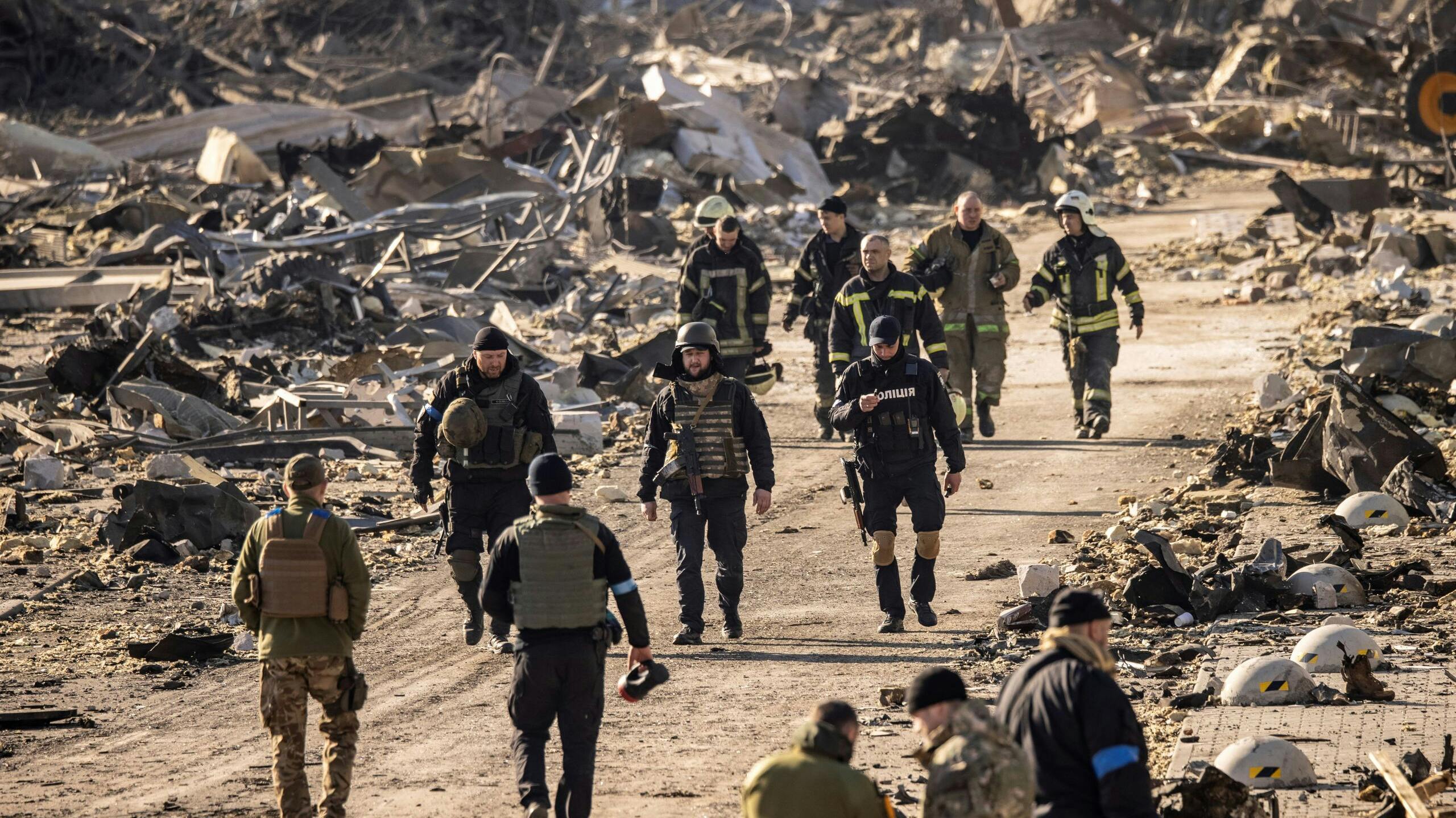 Reddingswerkers en militairen lopen rond in een gebied dat net gebombardeerd is. 