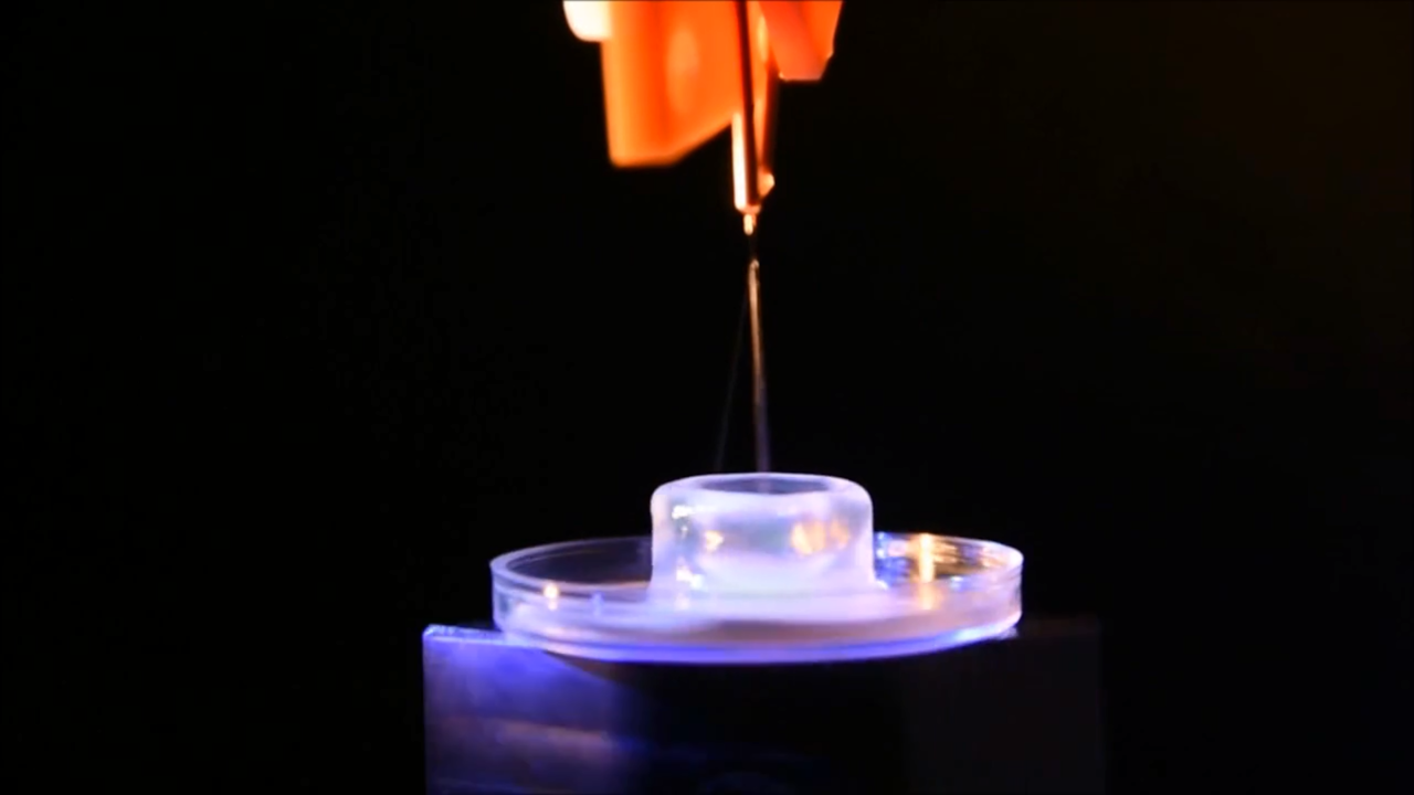 Screenshot van de video die de Universiteit Twente over de nieuwe biologische 3D-printer maakte. Links van de straal is een heel dun tweede straaltje zichtbaar. Dat zijn de druppeltjes waarmee geprint wordt.