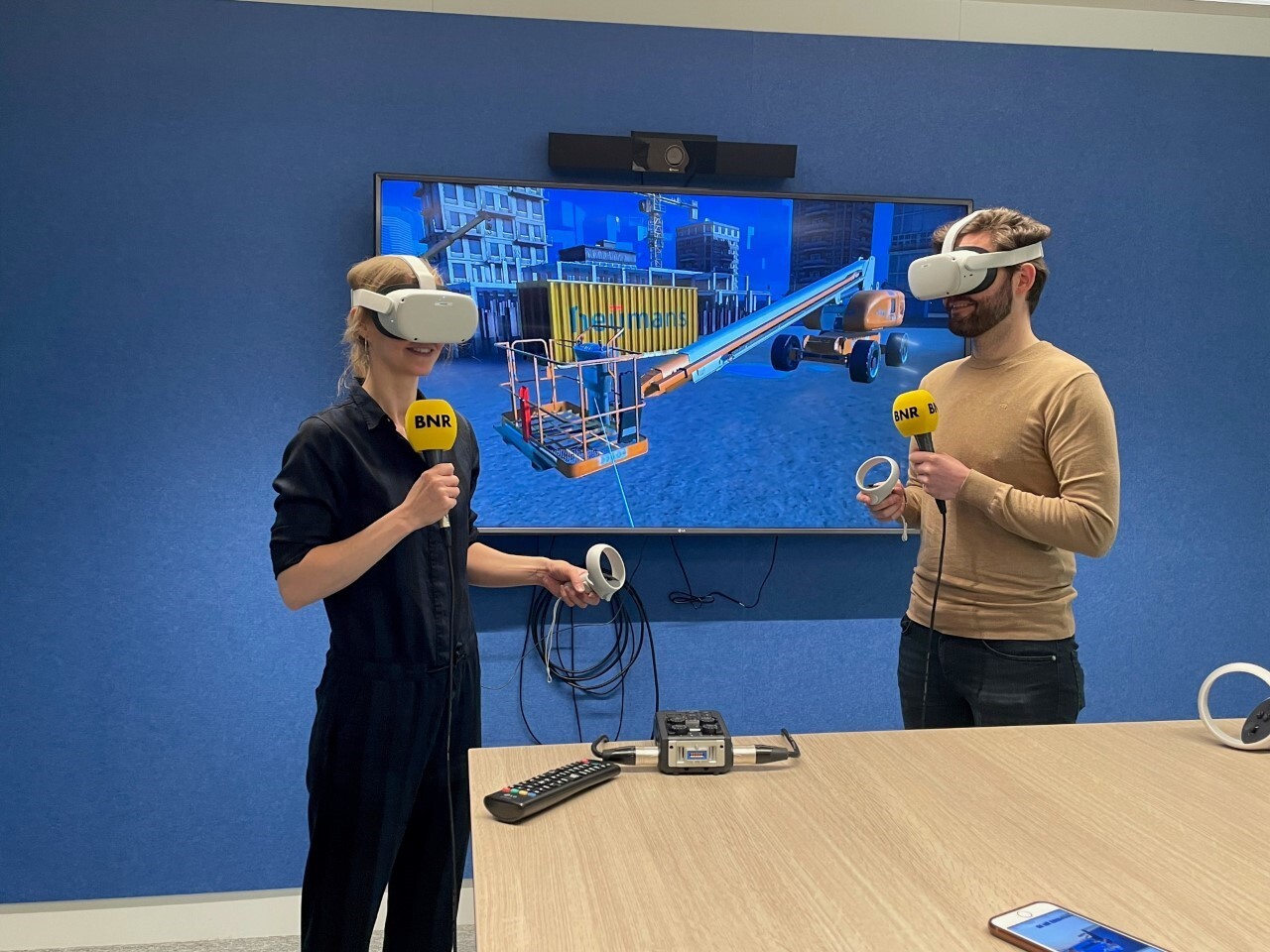 Presentator Karlijn Meinders in Virtual Reality hoe ze een hoogwerker moet besturen. Thomas Smits, adviseur bij Heijmans, helpt haar op weg.