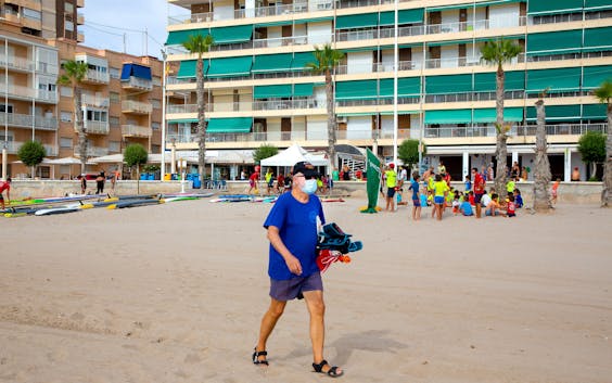 Een oudere man loopt met een mondkapje over het strand van El Campello aan de Costa Blanca in Spanje.