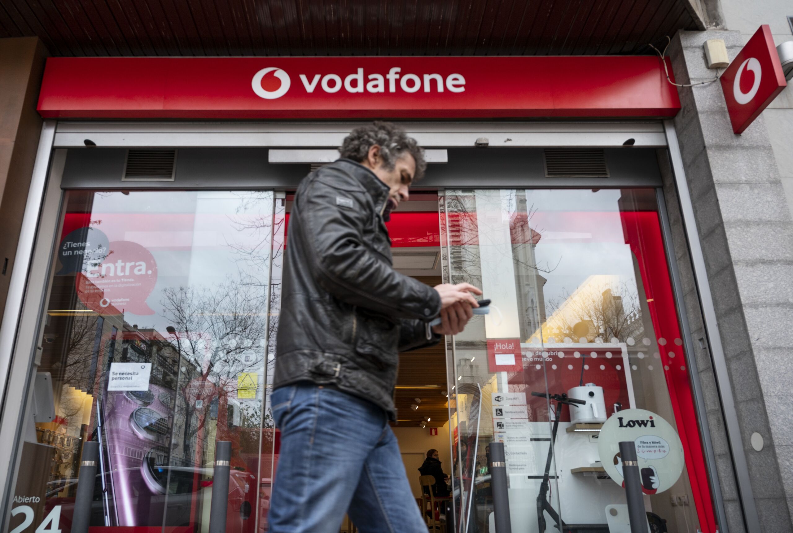 Voetganger gebruikt zijn telefoon voor een Vodafone winkel
