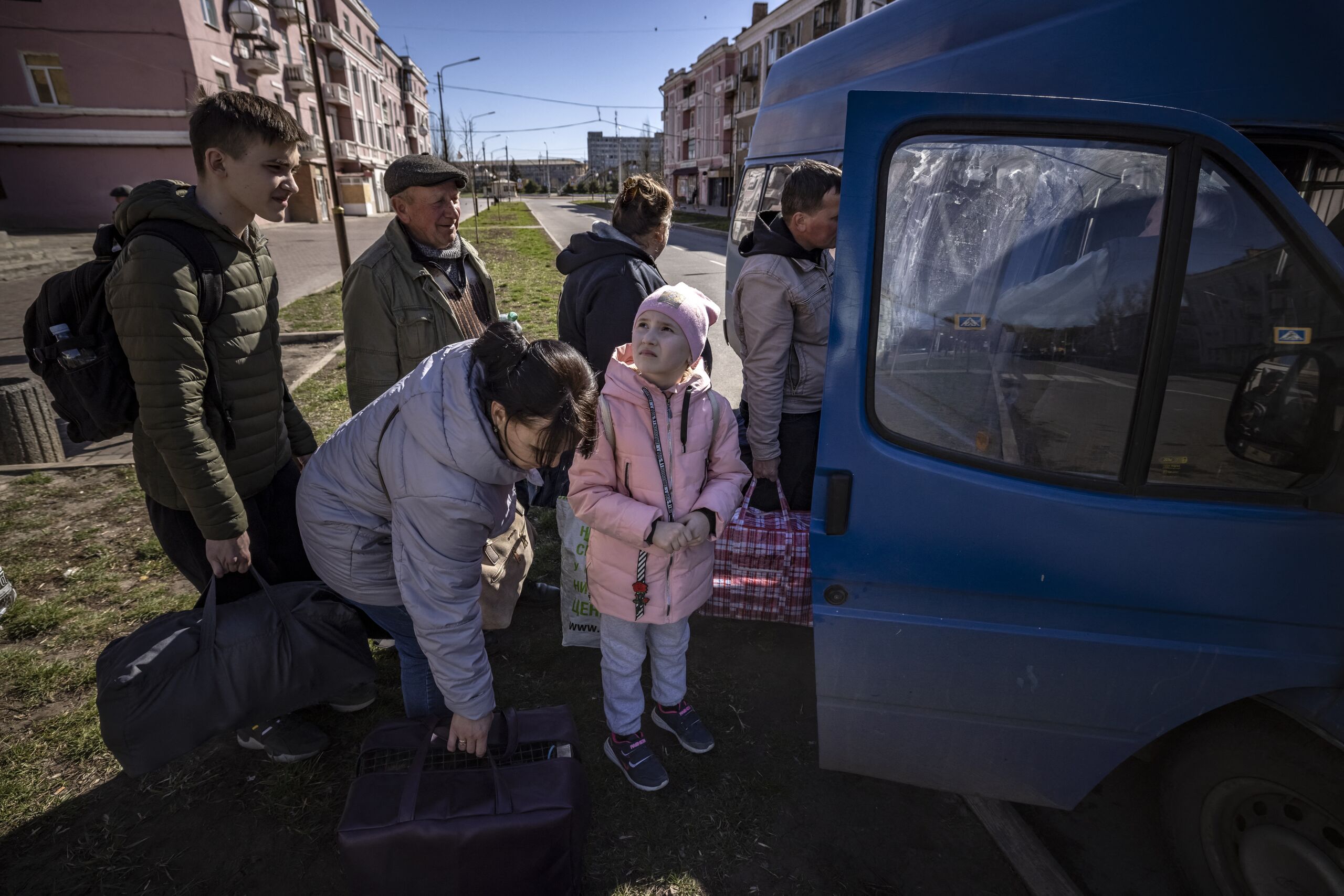 People wait for a bus as a children looks at the sky, a day after a rocket attack at a train station, in Kramatorsk, on April 9, 2022. At least 52 people were killed, including five children, following a rocket attack on April 8 on a train station in the eastern Ukrainian city of Kramatorsk that is being used for civilian evacuations, according to Donetsk region governor. FADEL SENNA / AFP