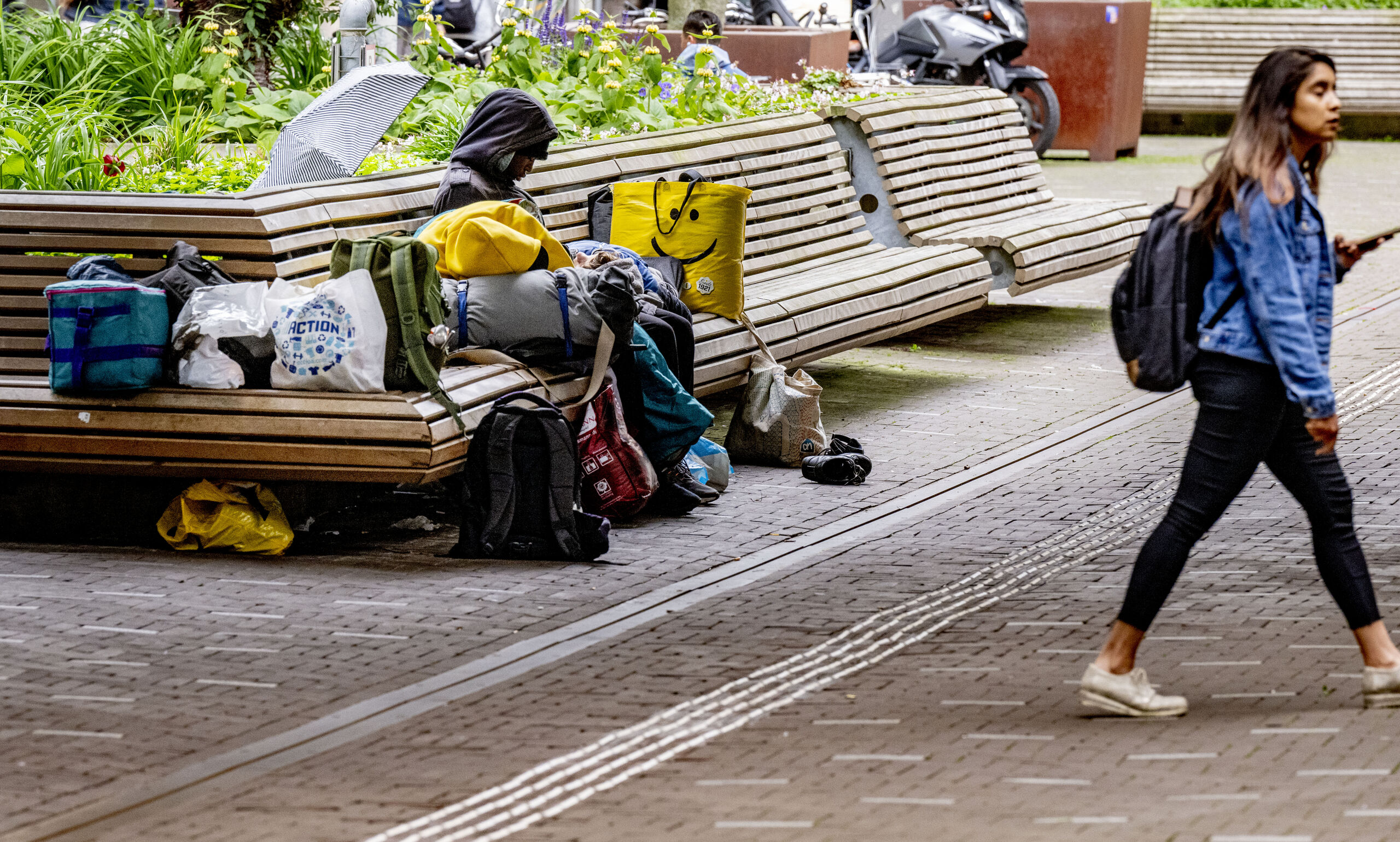 Een dakloze man ligt op straat op een bankje te slapen