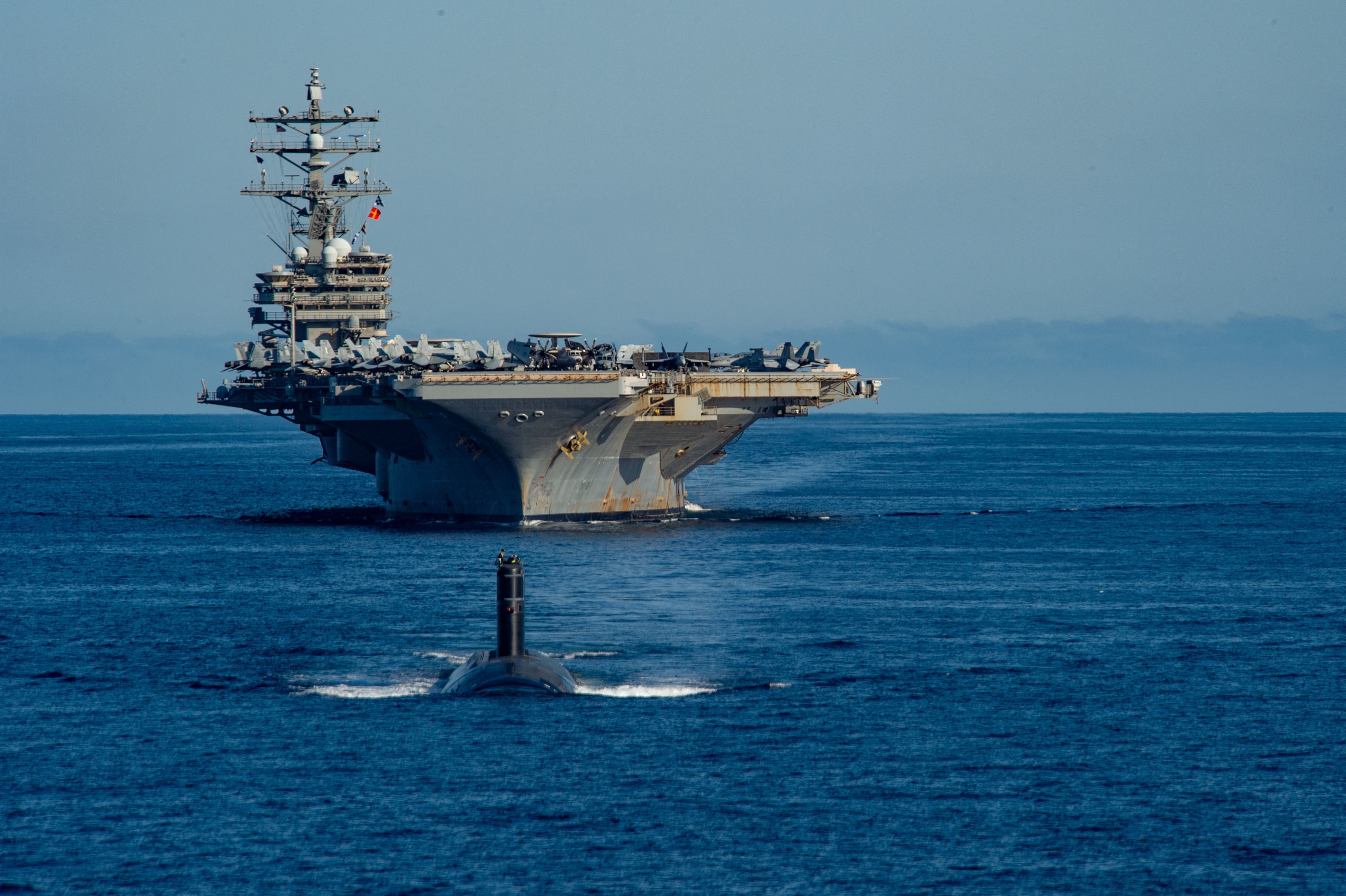 The USS Ronald Reagan with a submarine clearing the way.