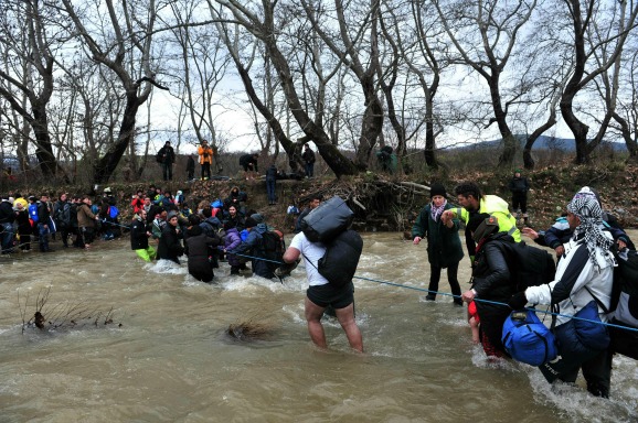Vluchtelingen steken de rivier bij de Grieks-Macedonische grens over. Foto ANP
