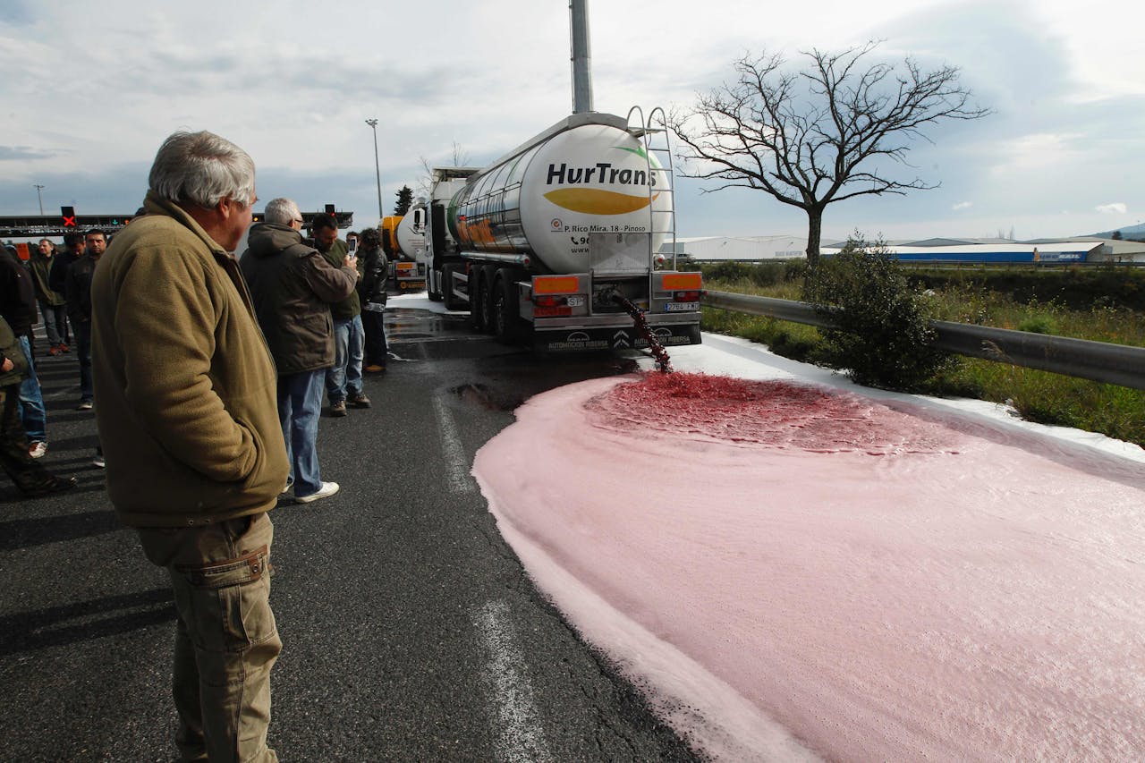 Franse wijnboeren kijken toe hoe een tanker met Spaanse wijn leegloopt op de snelweg. Foto AFP