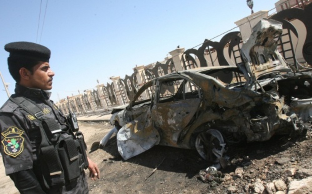 Een Iraakse politieagent kijkt naar een auto die getroffen is door een autobom. EPA