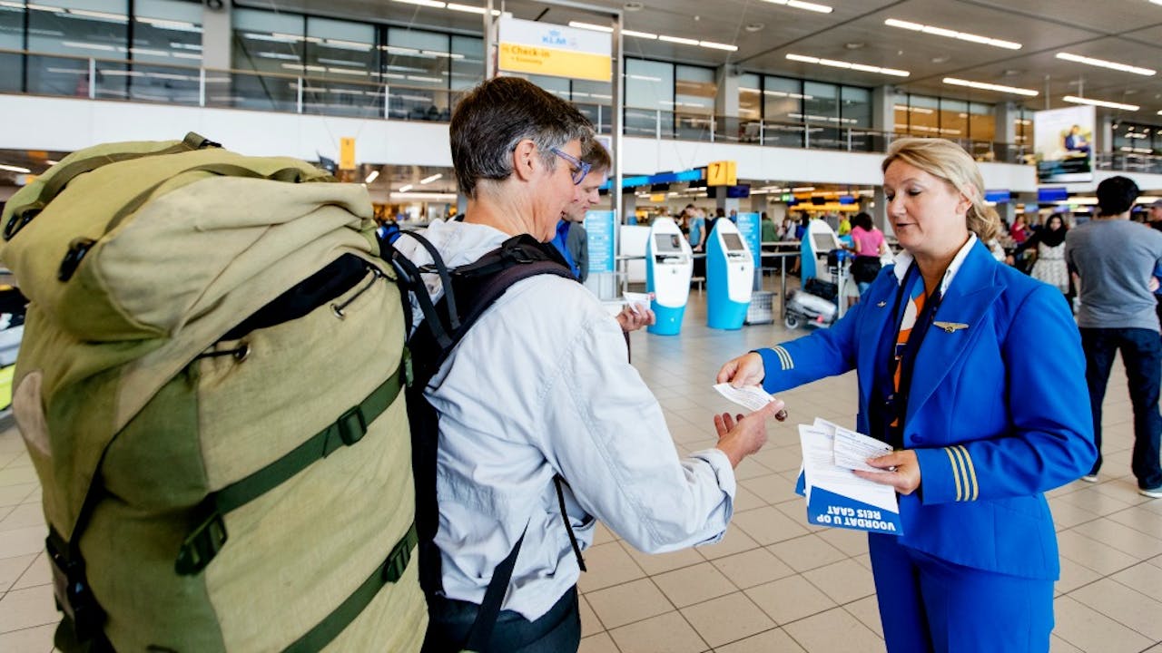 Een medewerker van KLM deelt flyers uit aan passagiers. Foto ANP