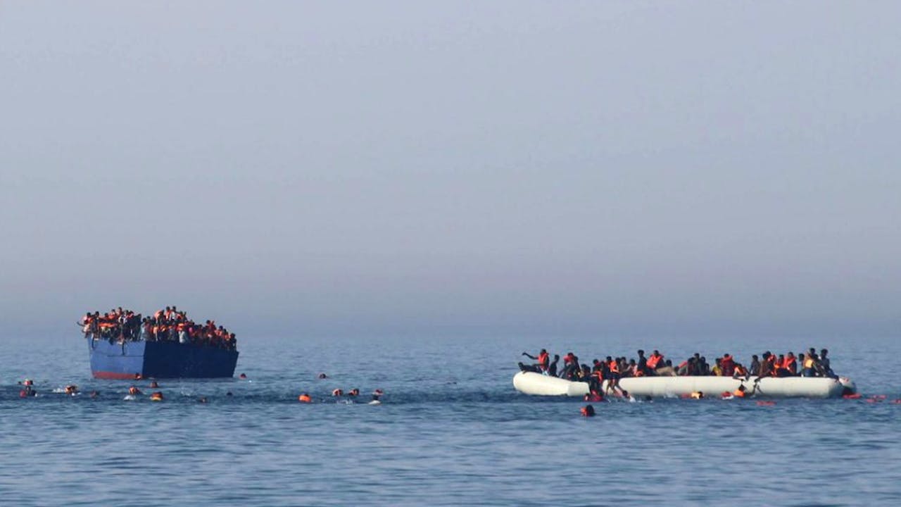 Migranten zwemmen weg van hun zinkende schip vlak voor een reddingsoperatie voor de Libische kust. Foto: ANP/AFP