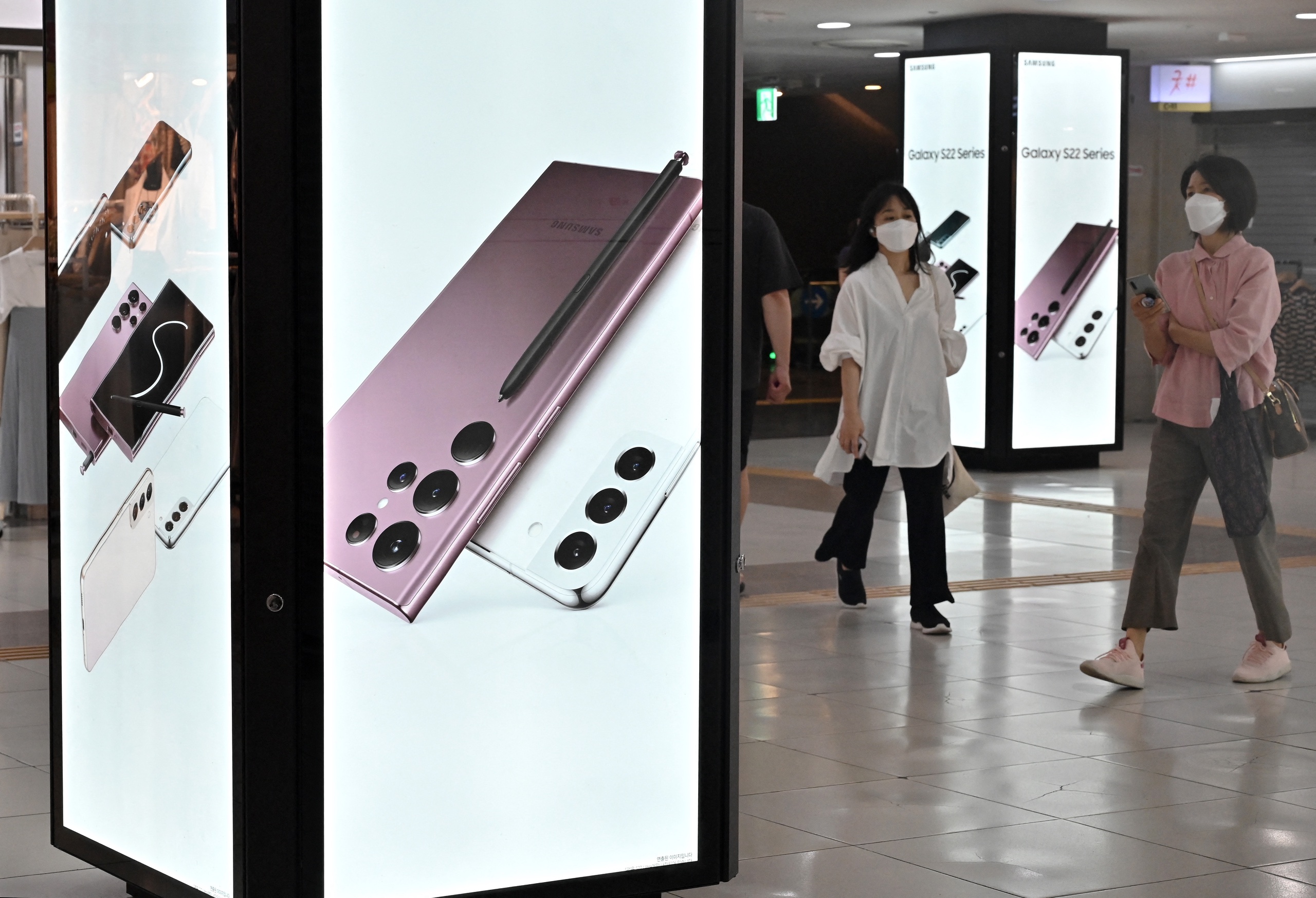 People walk past an advertisement for the Samsung Galaxy S22 smartphone at a Seoul subway station.