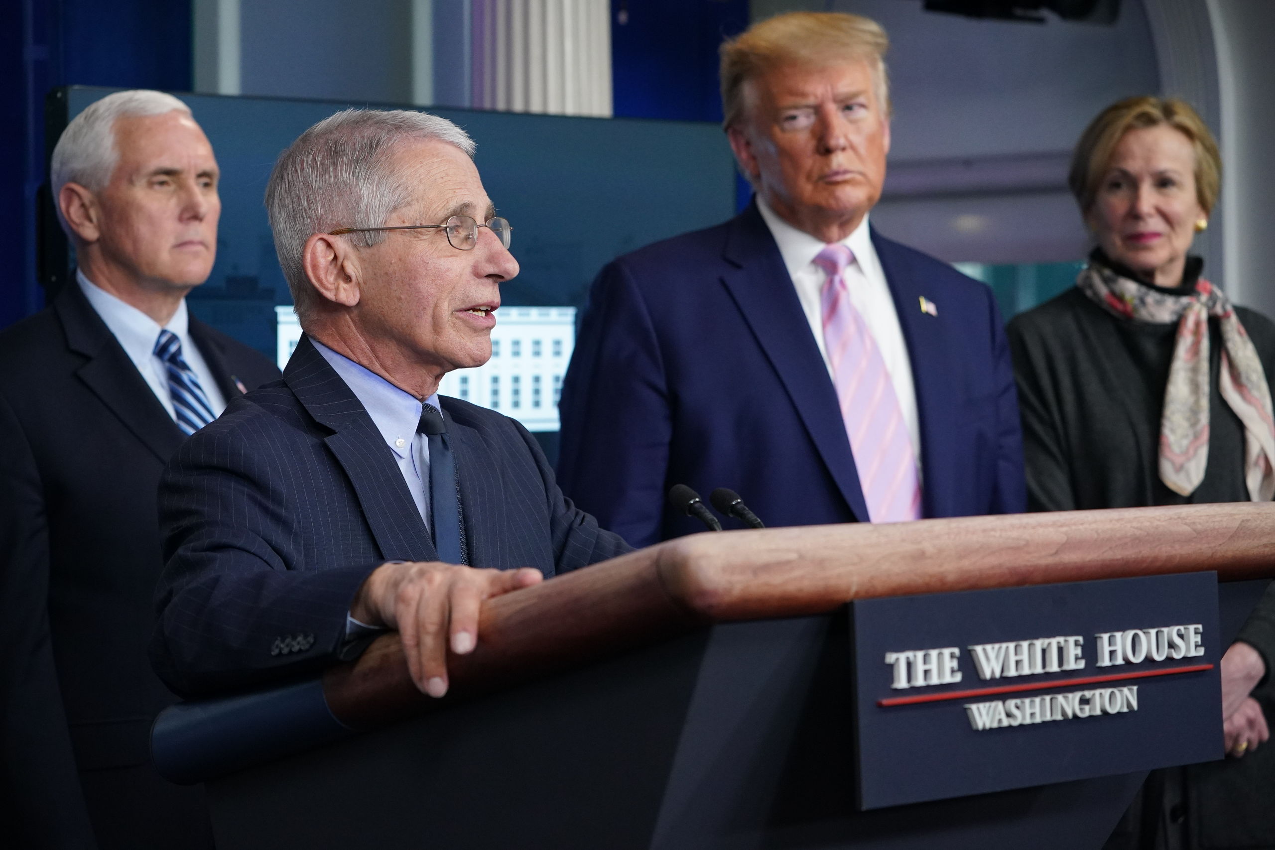 Donald Trump kijkt toe hoe zijn 'coronadokter' Fauci de pers toespreekt.