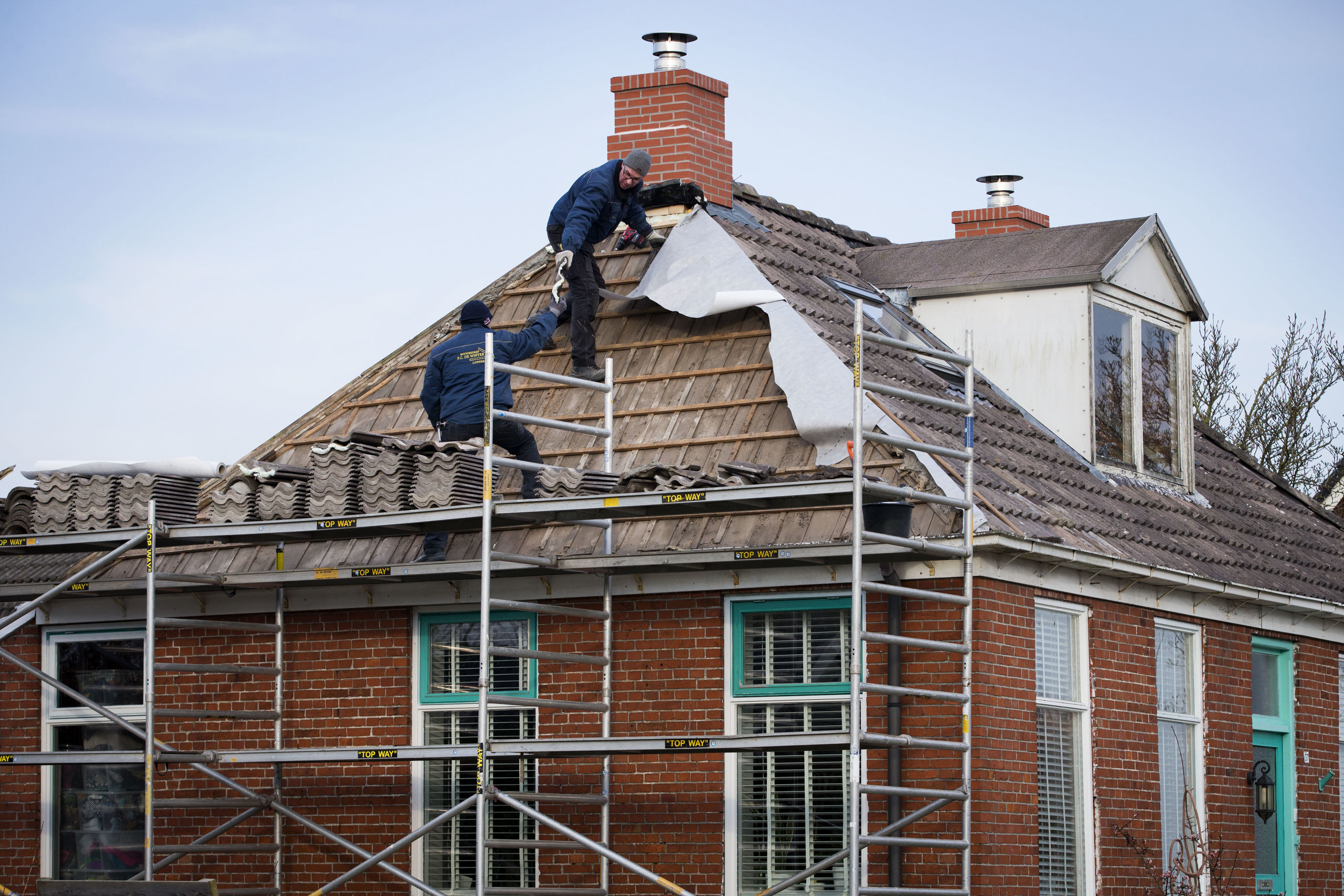 Bouwvakkers herstellen aardbevingsschade aan een schoorsteen van een huis in het Groningse dorp 't Zandt. 
