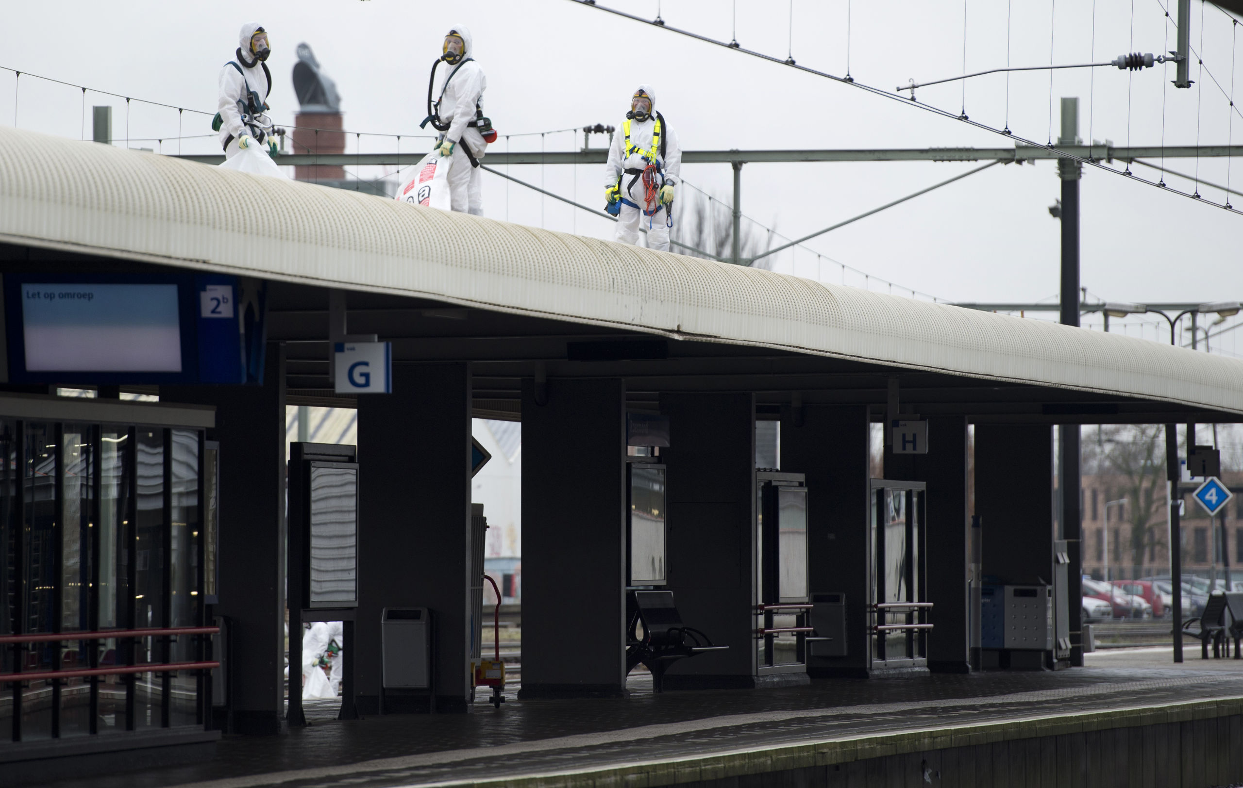 Witte pakken van asbestbestrijders op een stationsdak in Roermond. 