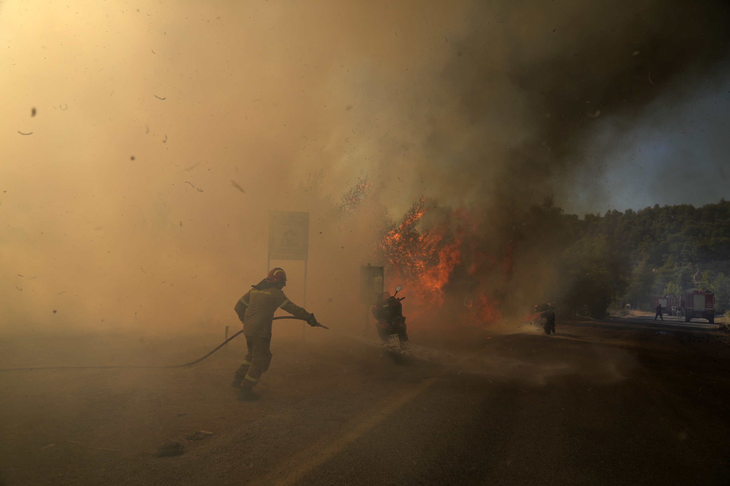 A firefighter tries to extinguish the flames next to motorcycles during a wildfire near Megara town, west of Athens, Greece, Wednesday, July 20, 2022. The new fire broke out in the hills outside the town of Megara, 40 kilometers (25 miles) to the west, prompting a new, but more limited, round of evacuations. (AP Photo/Petros Giannakouris)