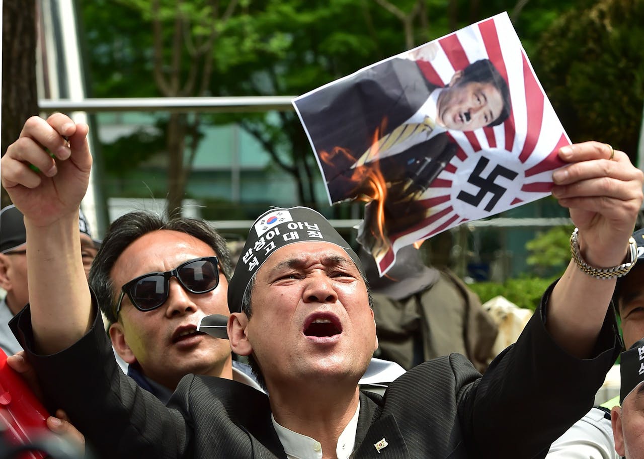 A South Korean activist burns a poster showing a picture of Japan's Prime Minister Shinzo Abe depicted as former German chancellor Adolf Hitler.