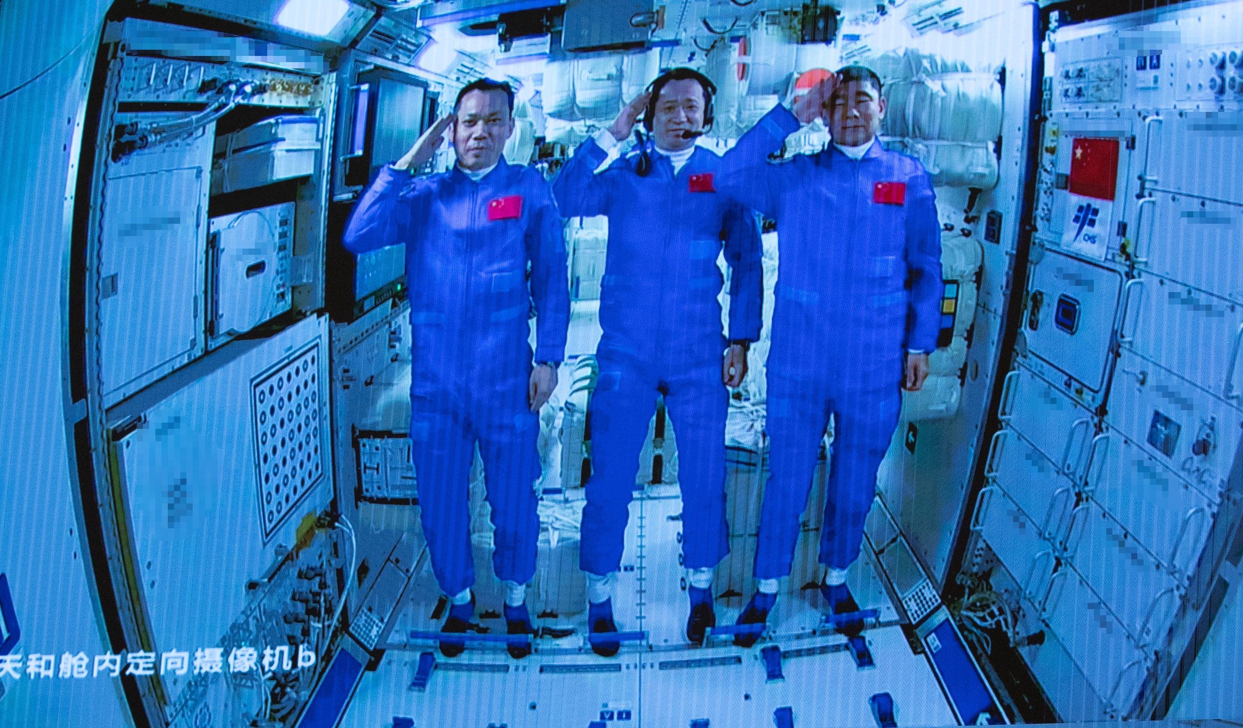 Drie Chinese astronauten aan boord van het Shenzhou-12 ruimteschip die salueren na het binnengaan van de kernmodule van het ruimtestation Tianhe. 